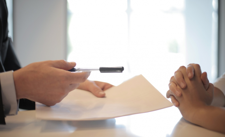a businessperson handing a pen and contract to another person