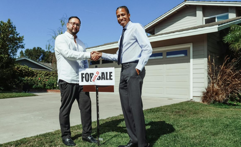 People shaking hands in front of a renovated home with a "Sold" sign