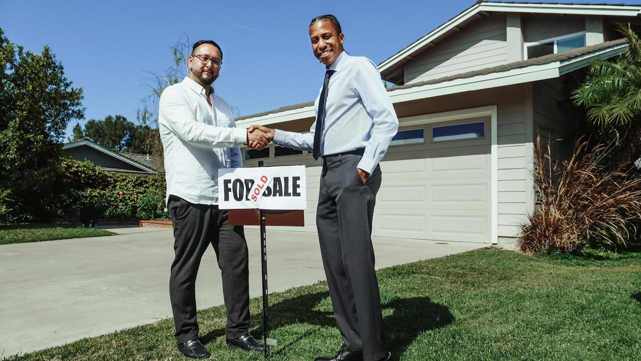 People shaking hands in front of a renovated home with a "Sold" sign