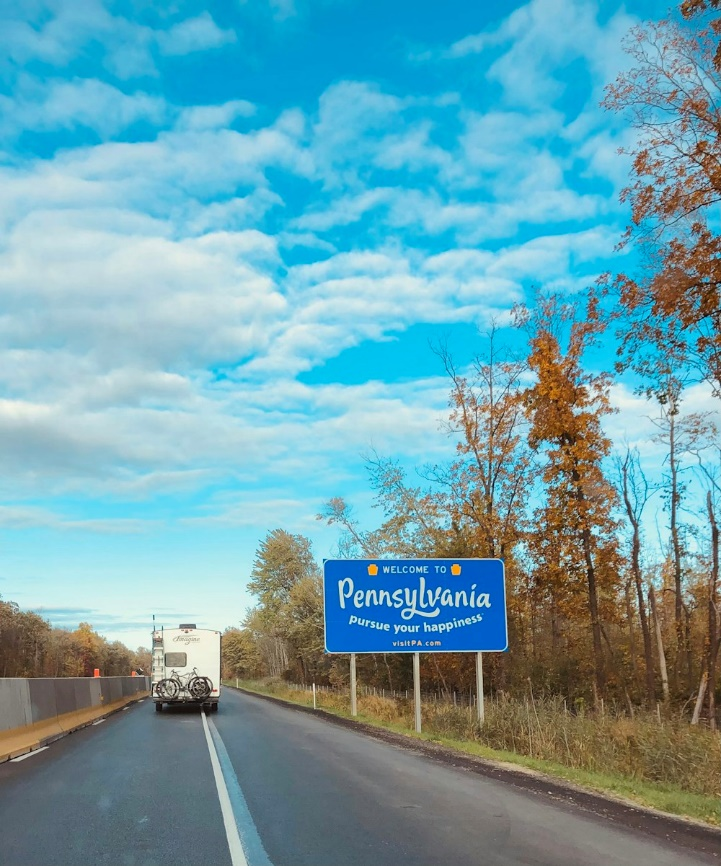 A blue and white welcome sign for the state of Pennsylvania with mountains in the background.