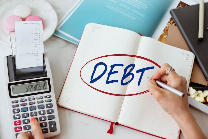 A person working on a calculator with a pen in the other hand and debt written with a red circle on a notepad