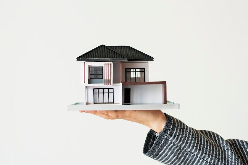 A hand holding a model house for a home loan campaign