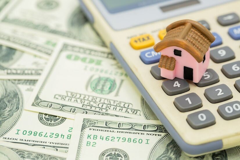 An image of a miniature house model on a calculator on top of 100 US dollar banknotes
