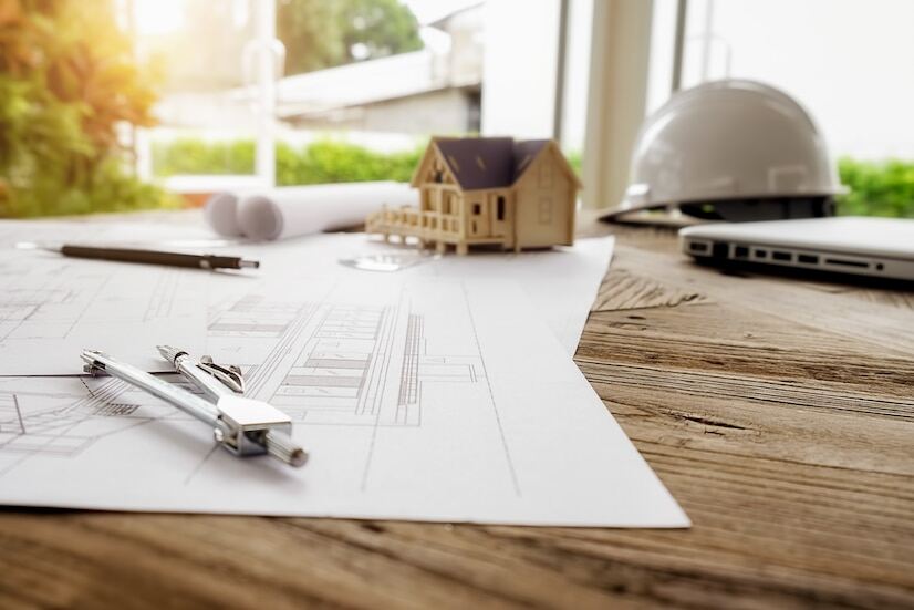 An image of a construction plan, a compass, a miniature house, and a safety hat