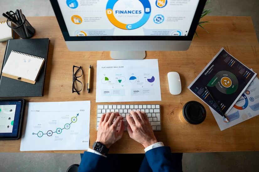 An image of a person working on a computer with financial details open and some documents