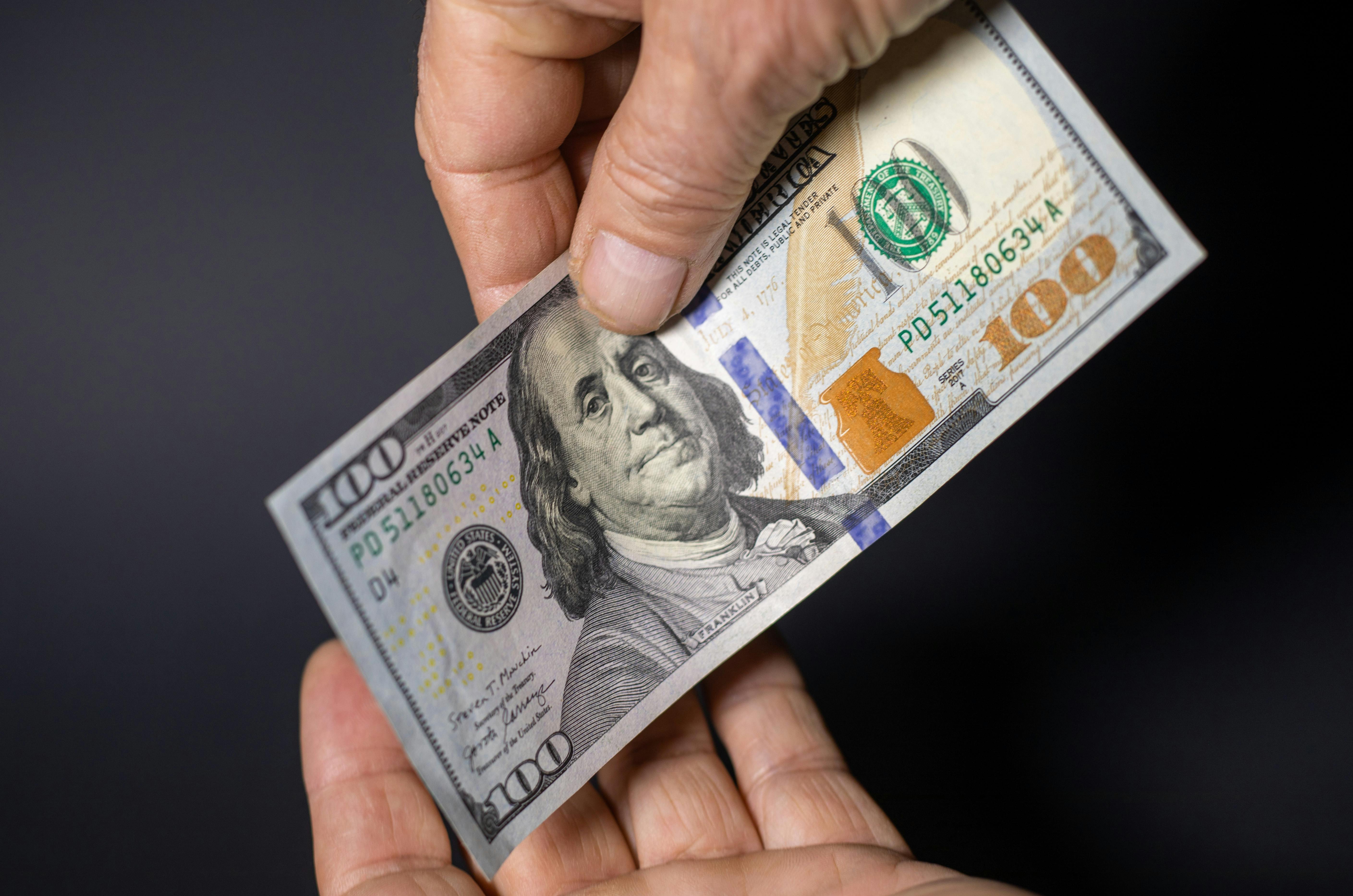 Two people exchanging a 100 US dollar banknote