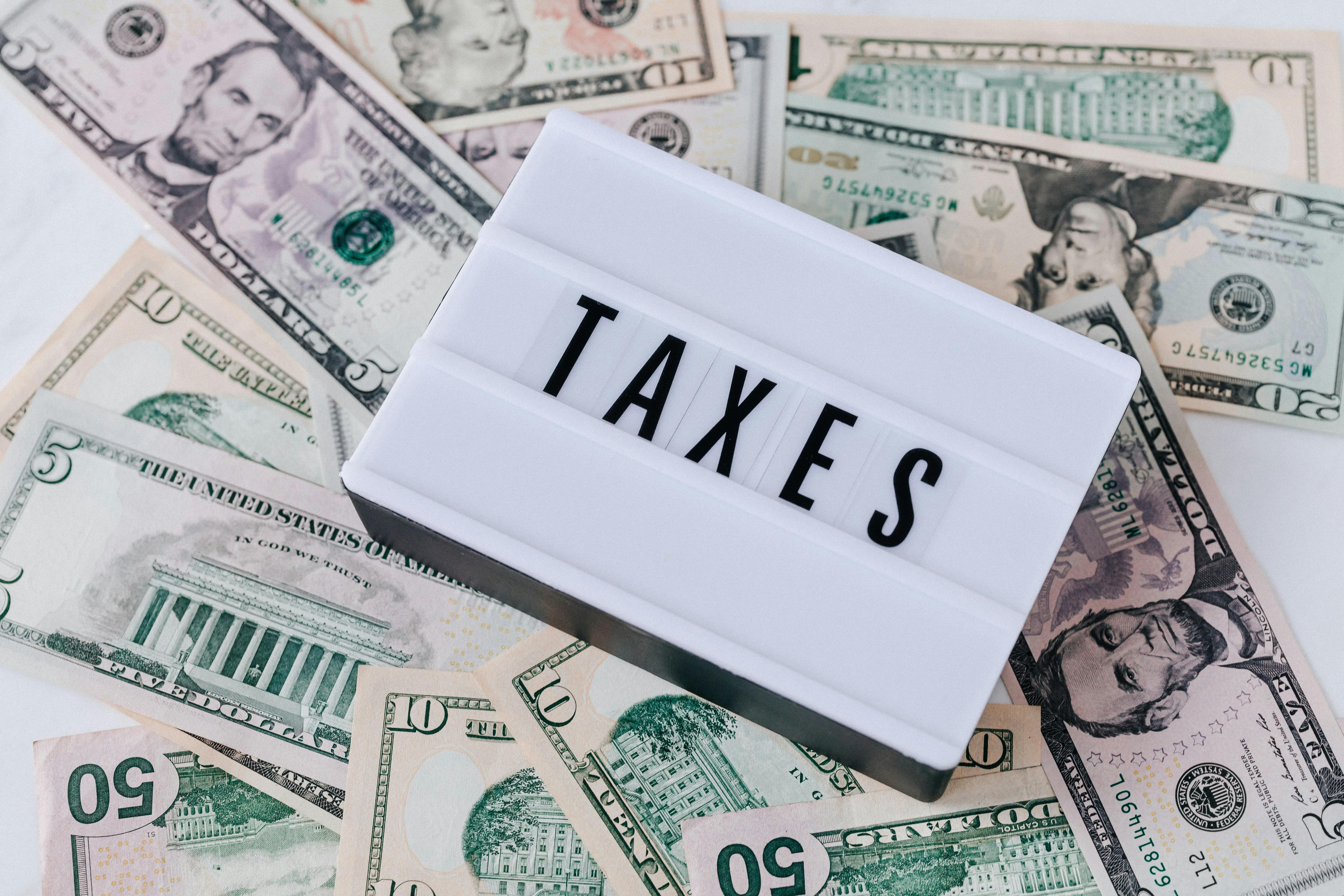 A quote board with “Tax” written on it on top of US dollar banknotes