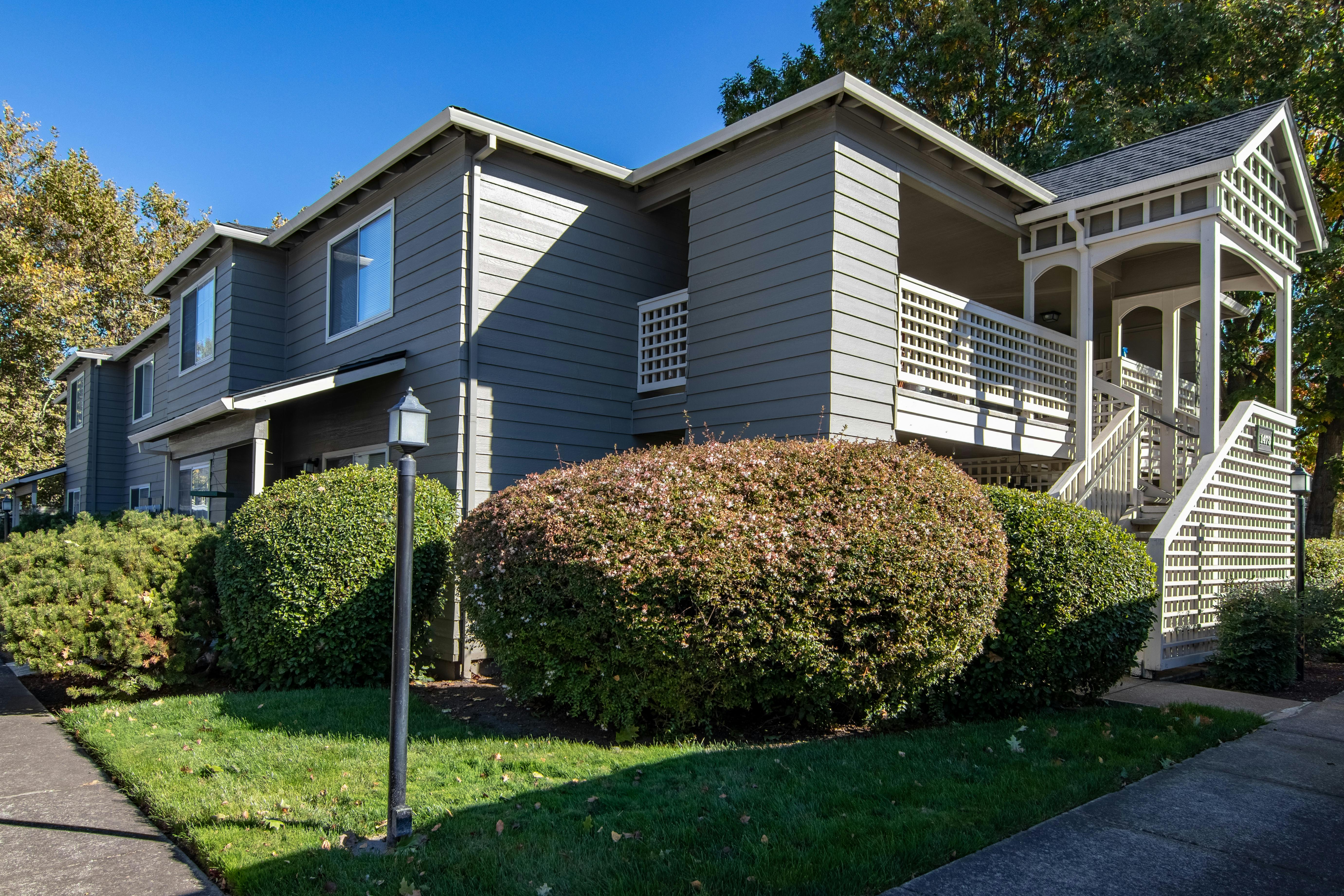 A grey real estate house with bushes in the lawn