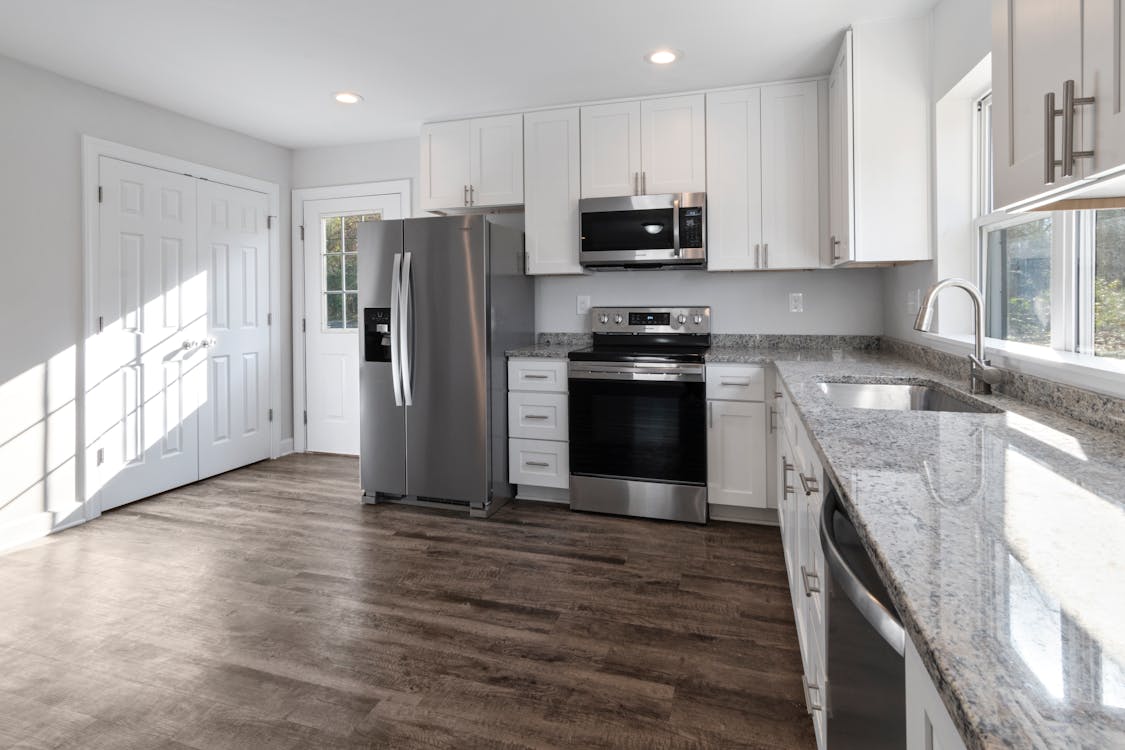 A kitchen design with white cabinets and wooden flooring