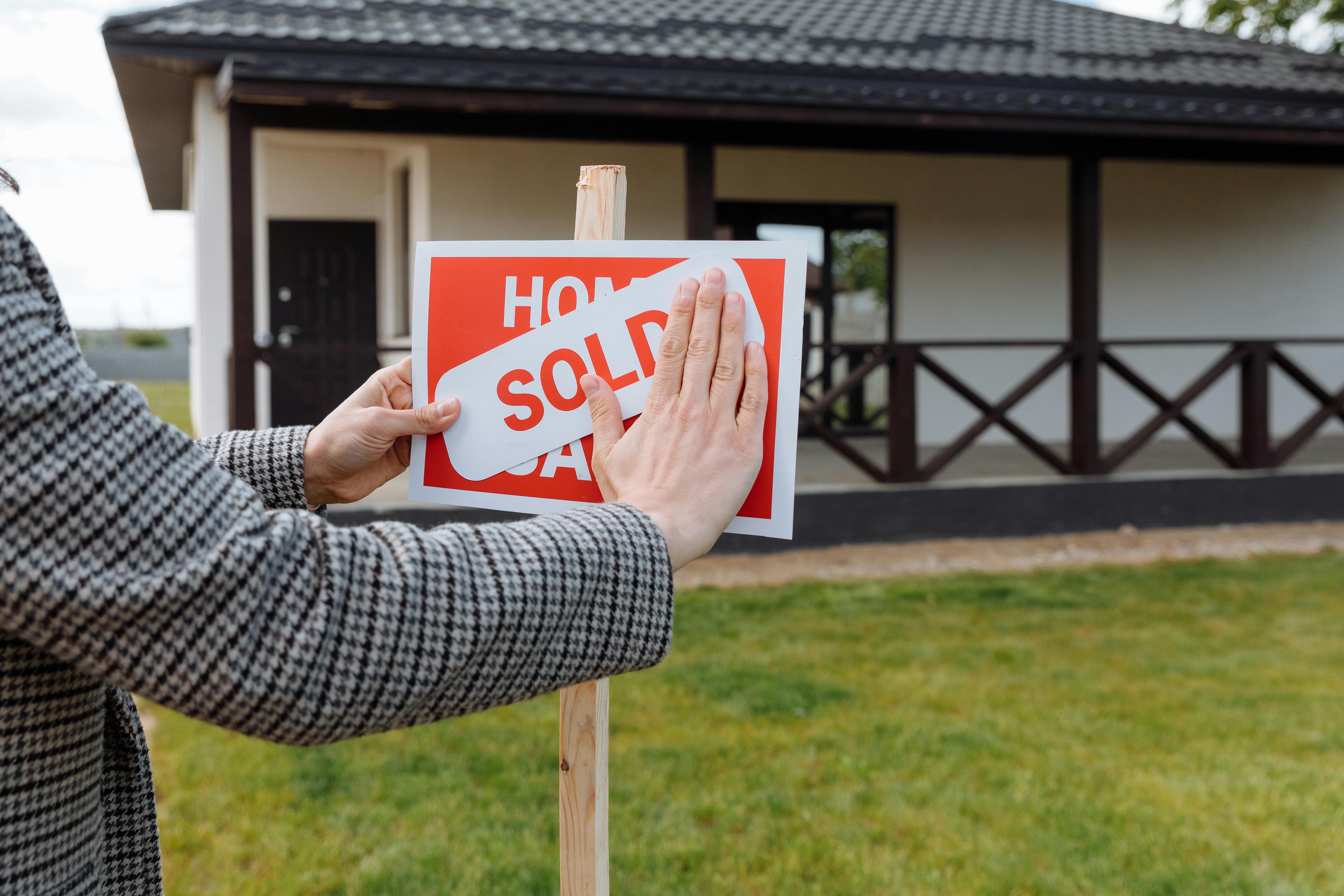 A closeup of a woman replacing House on Sale sign with Sold in front of a house