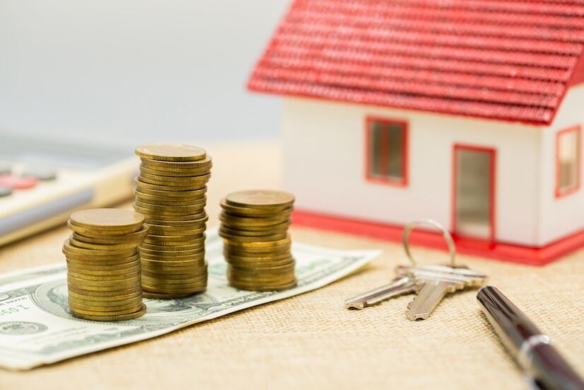 Three stacks of coins on a dollar note, a key, a pen, and a house model