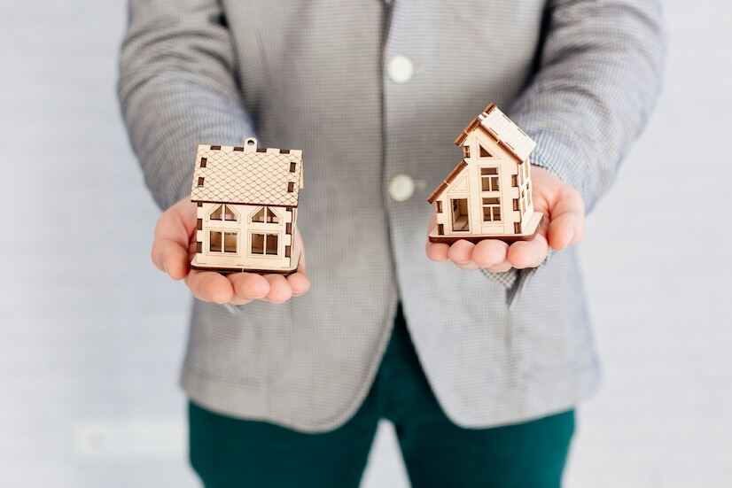 A closeup image of a person holding two miniature houses in his hand