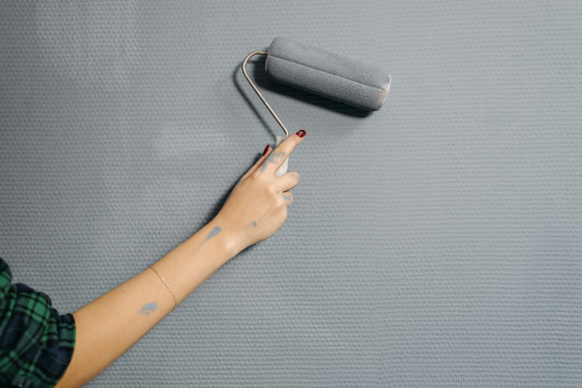 A person painting a wall grey using paint rollers