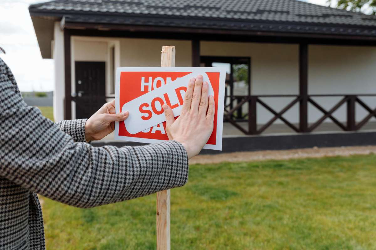 A closeup of a woman replacing House on Sale sign with Sold in front of a house