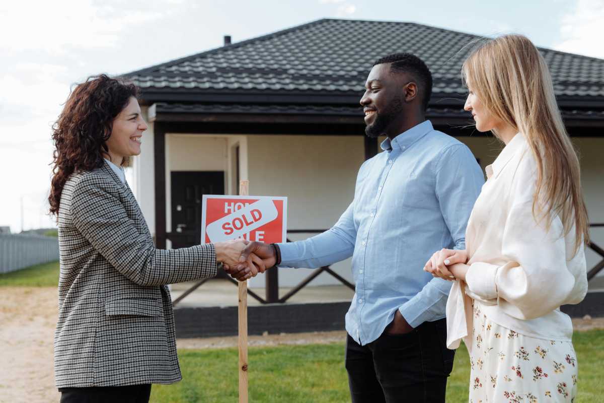  A real estate investor shaking hands with her clients near a “Sold” sign in front of a house 