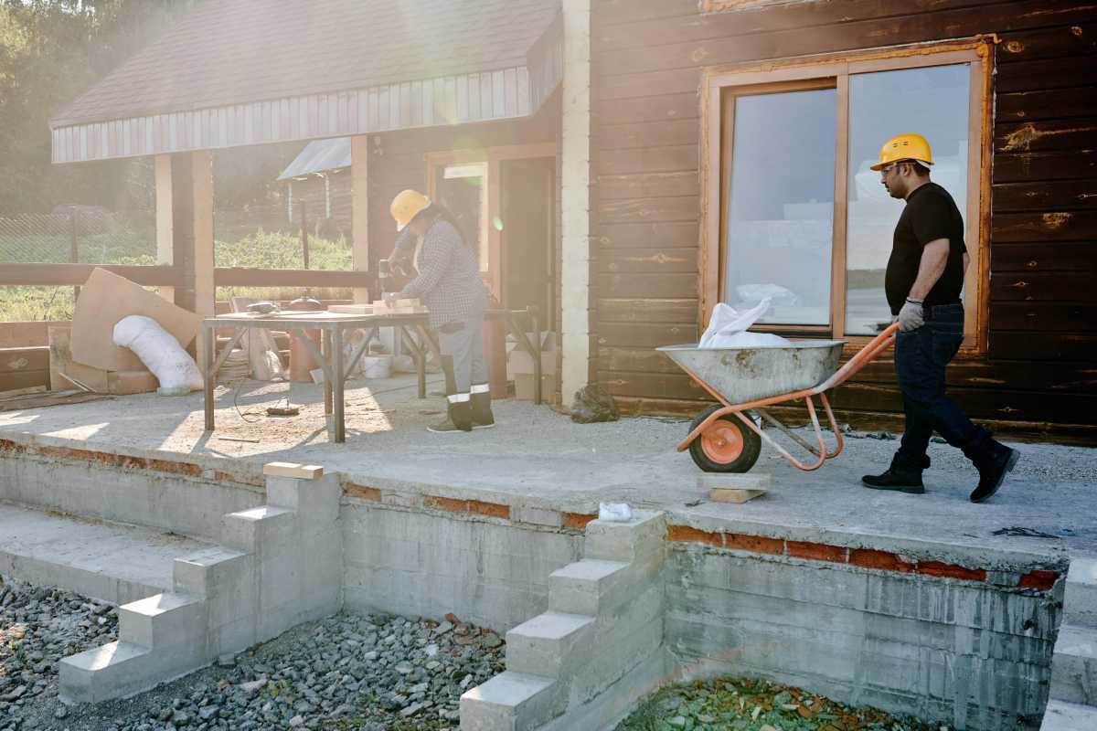 A Man in Black Shirt Holding a Gray and Orange Wheelbarrow at a residential building construction site